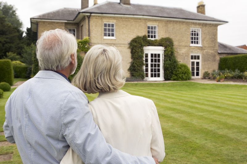 Old couple standing in front of their mansion that would be used for a jumbo reverse mortgage.