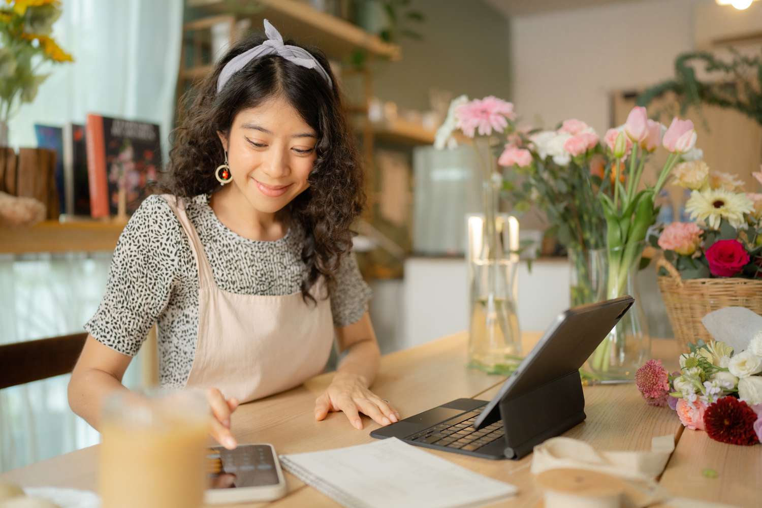 Flower shop owner calculating expenses and revenue on mobile phone to get a working ratio for the business.