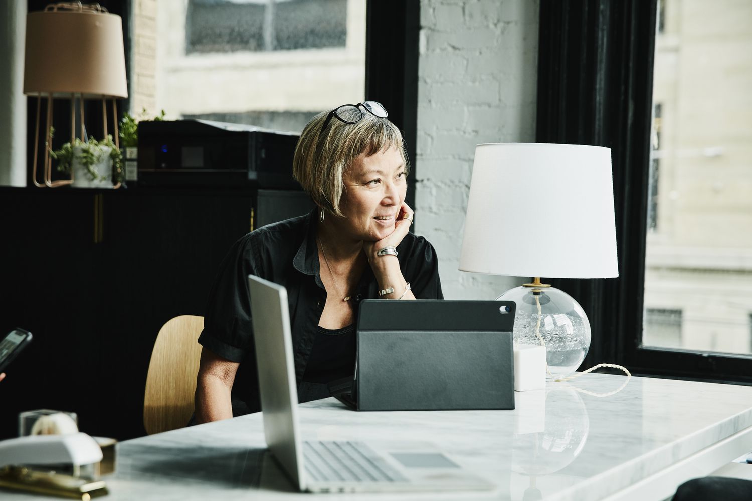 A woman sits at a desk with a device.
