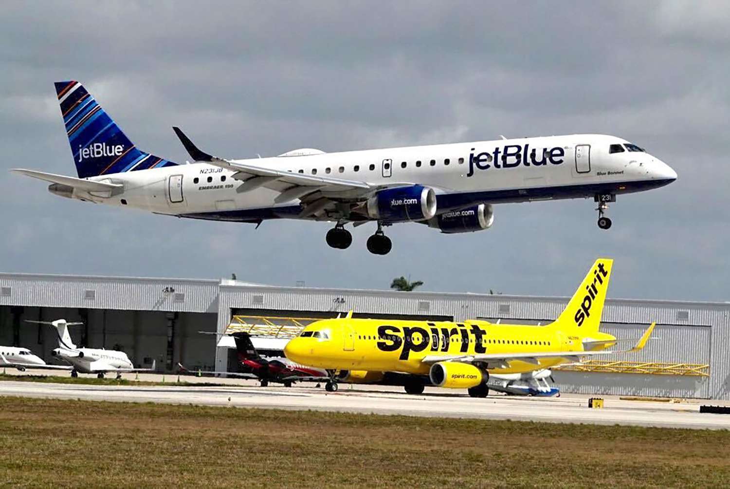A JetBlue airliner lands past a Spirit Airlines jet on taxi way at Fort Lauderdale Hollywood International Airport
