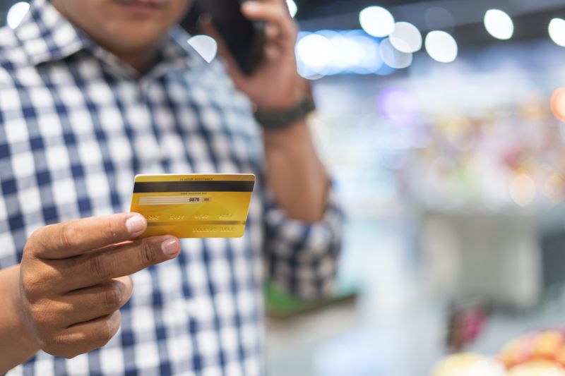 A shopper holding a credit card while talking on the phone, unable to tell whether it is a visa or a mastercard.