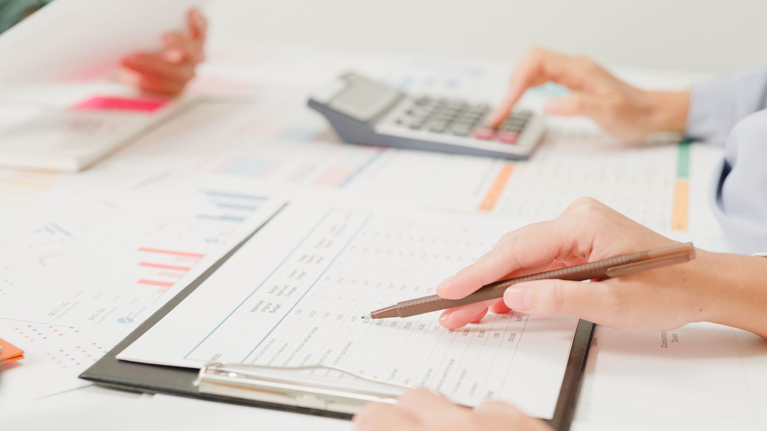A close-up of people at a table reviewing financial documents, while one person uses a calculator.