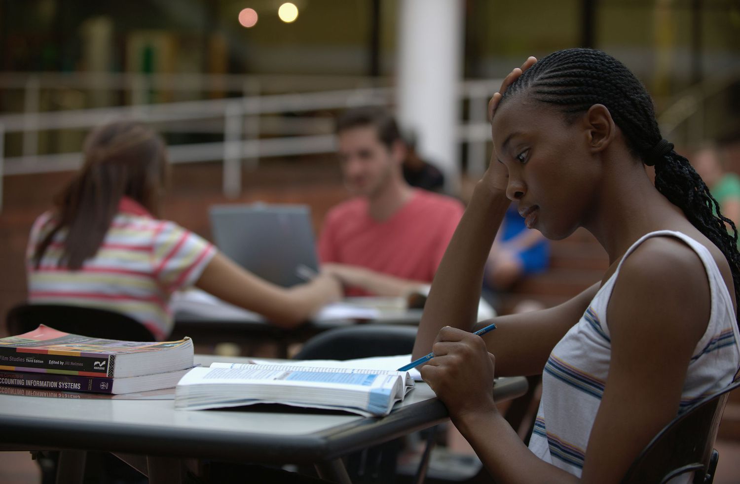 Female student studying with textbook with other students working at desks behind her.