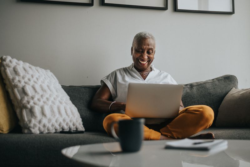 Smiling woman sitting on a couch and working on a laptop