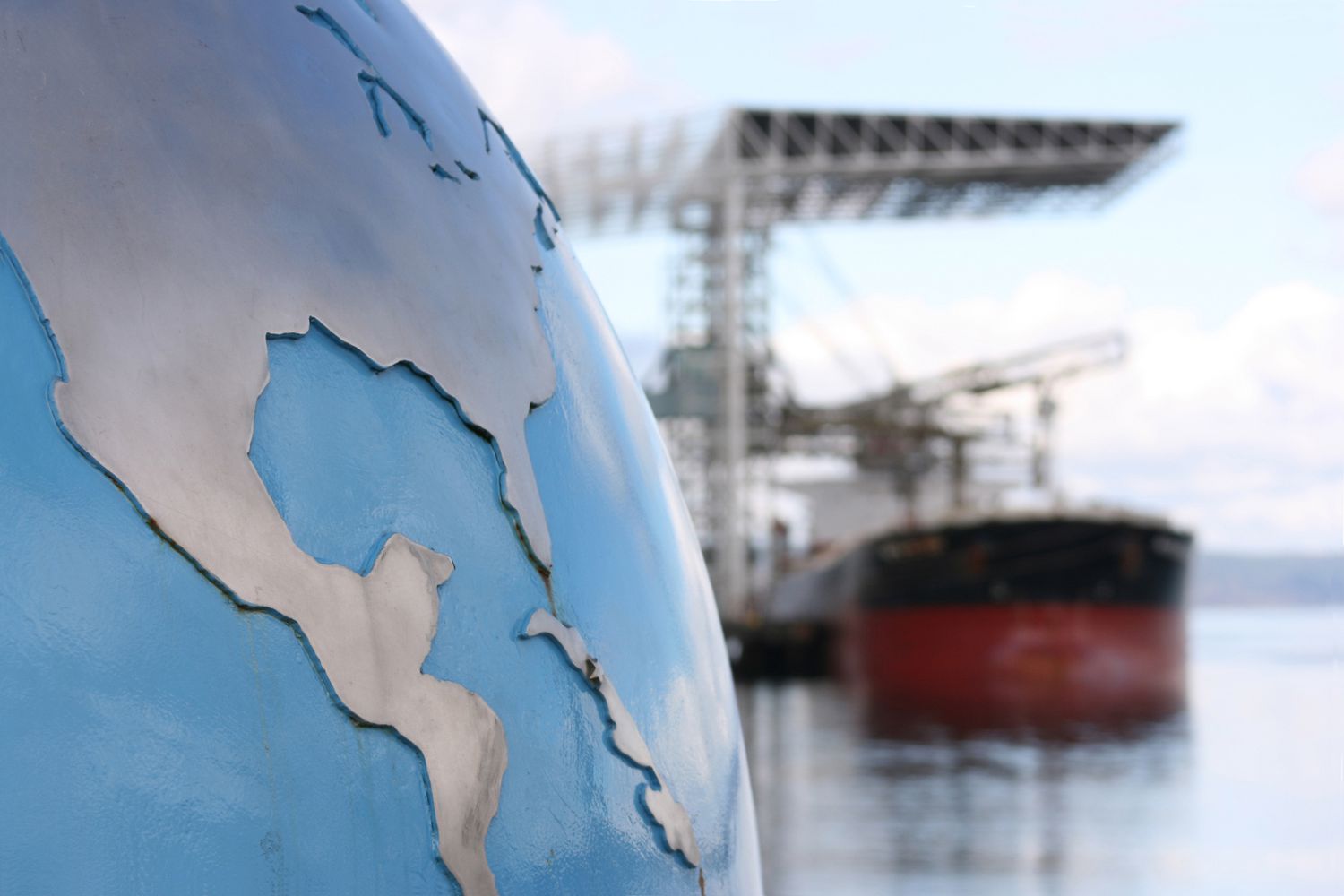 A globe with focus on the United States (USA) and Central America contrasted against a blurred background of a bulk cargo ship