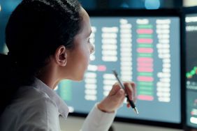Woman staring at computer screens with stock market information displayed
