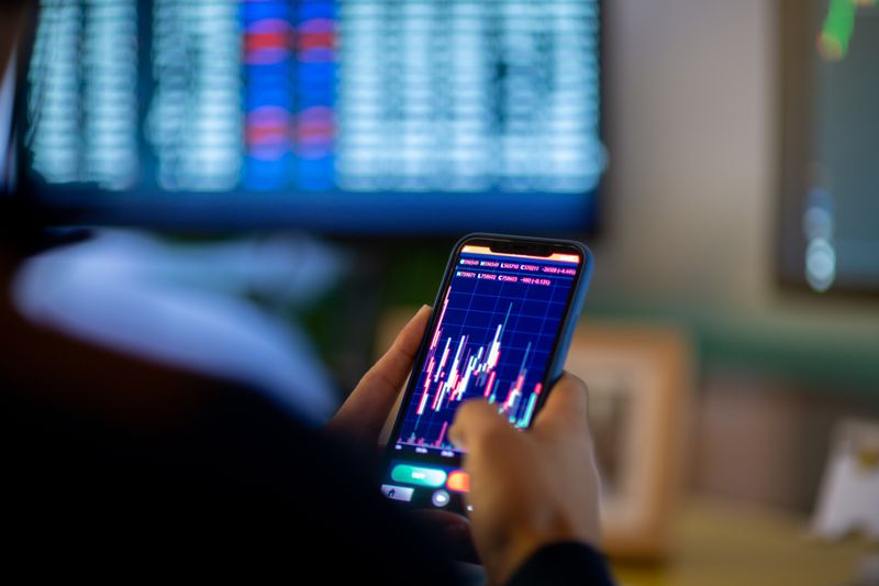 Person holding a cellphone, watching market trends. 