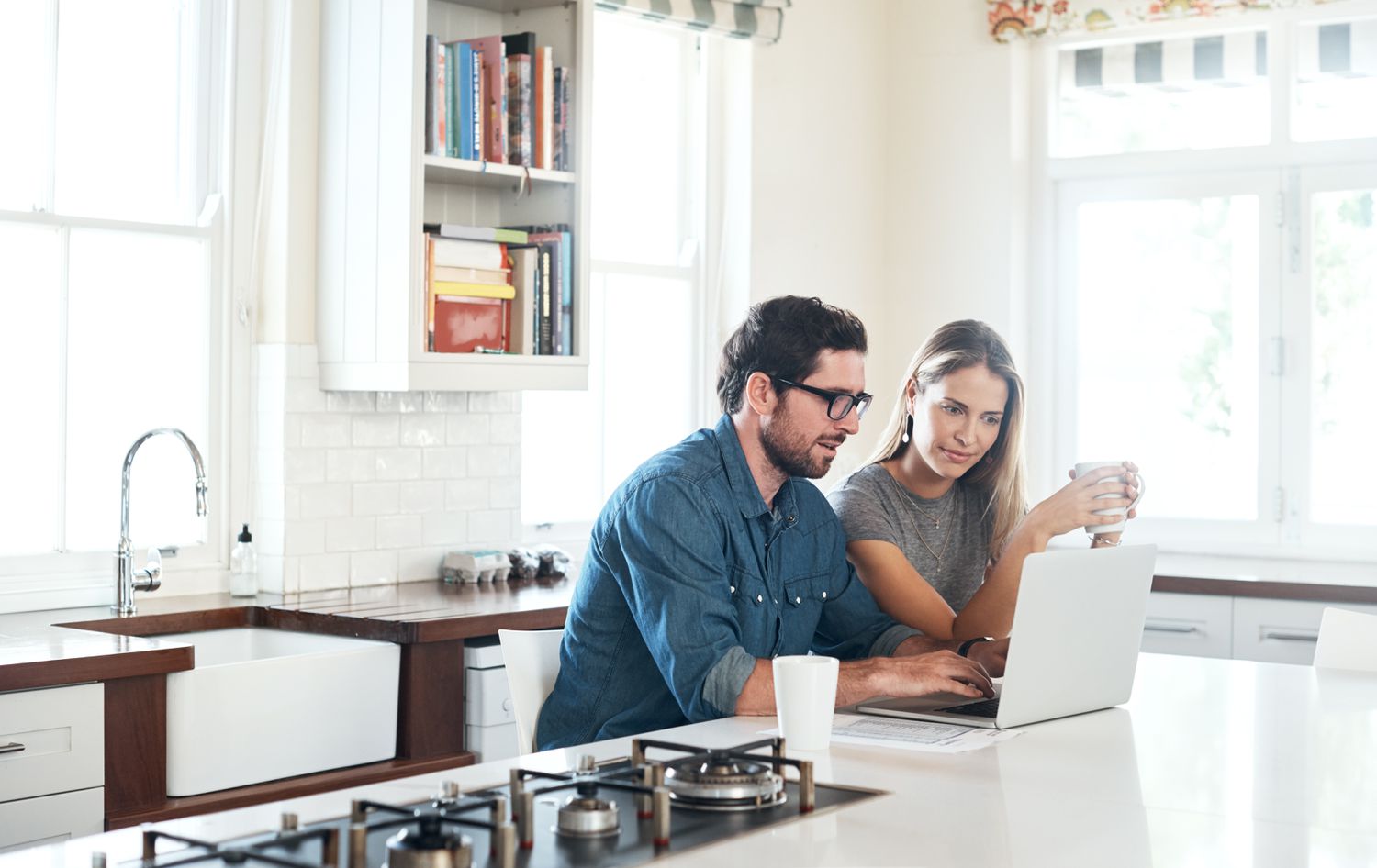 A man and a woman sit at a kitchen island with a laptop