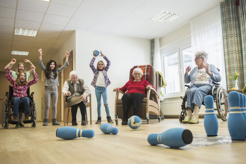 Girls playing bowling with senior women in rest home