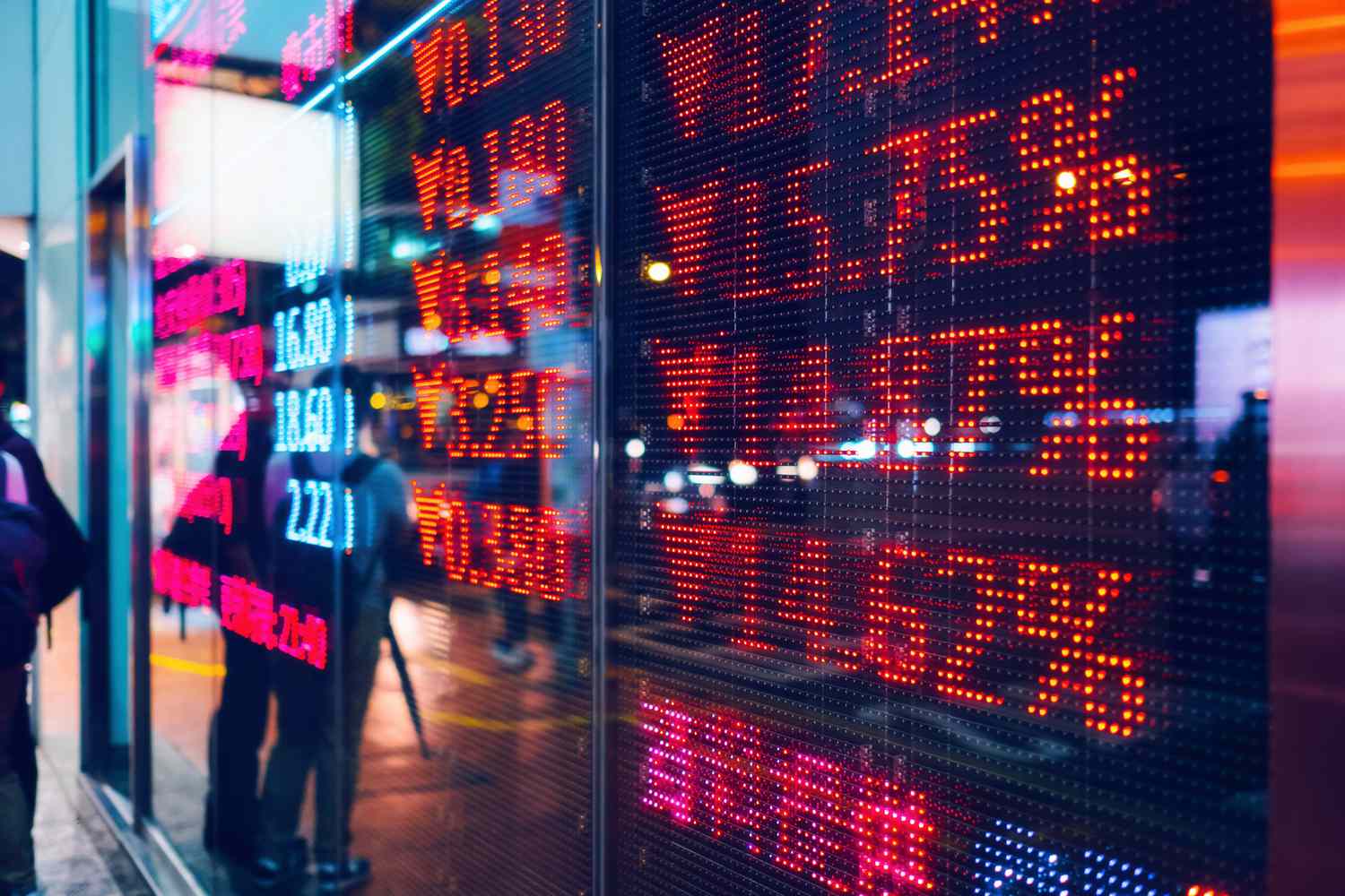 People standing outside at night in front of stock ticker sign
