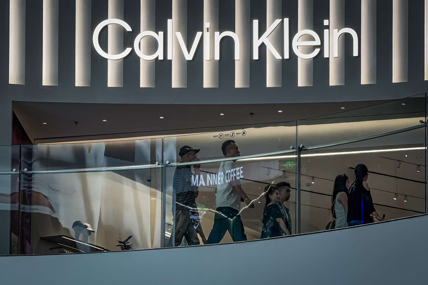 Shoppers walk past a Calvin Klein store beneath illuminated signage inside a modern shopping mall on May 20, 2025 in Chongqing, China