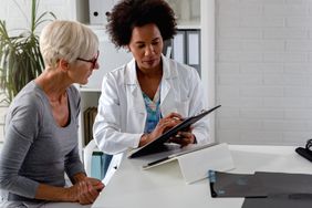 A female doctor sits at her desk and chats to an older female patient while looking at her test results