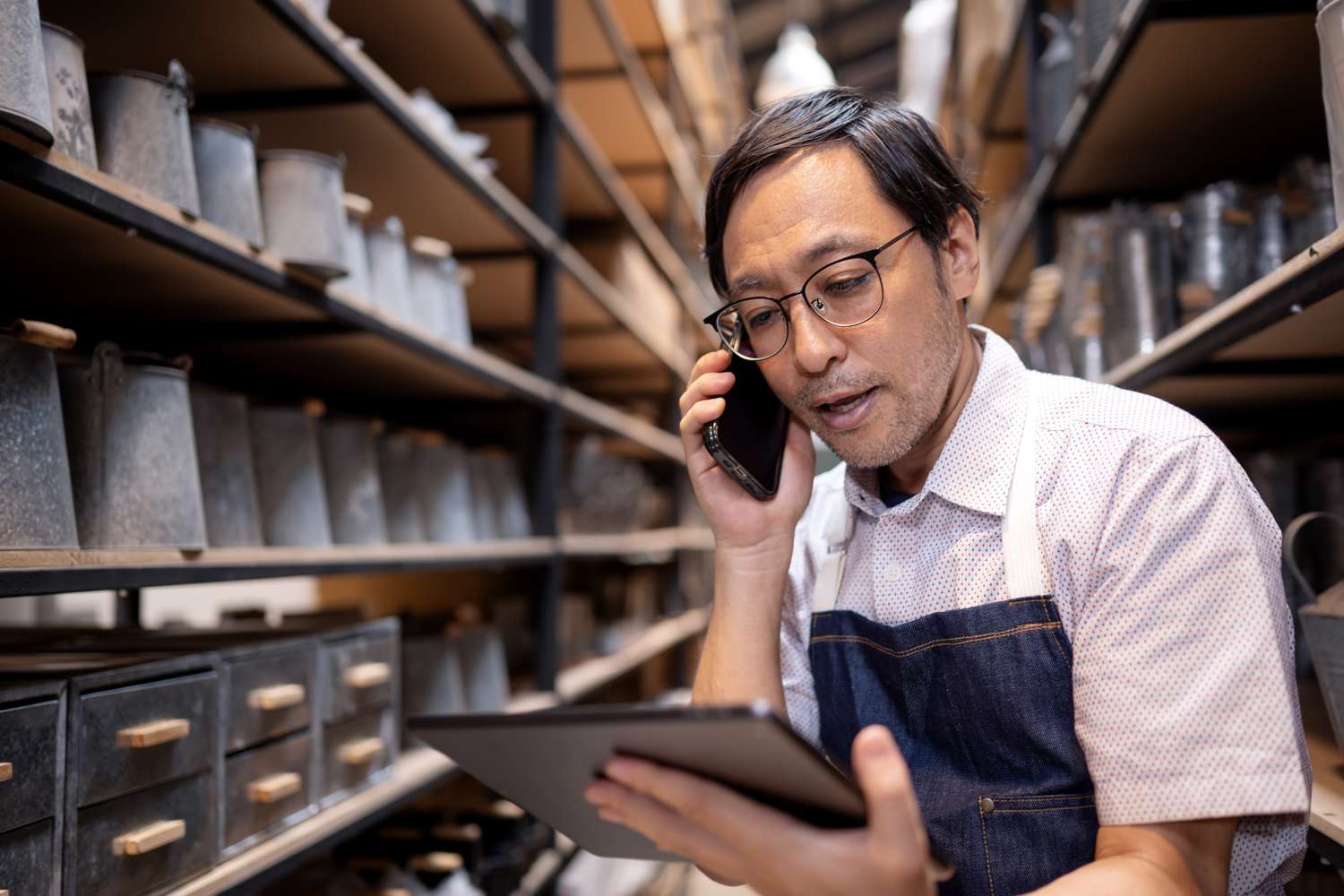 A man uses a smartphone to talk to a customer while looking at a tablet screen.