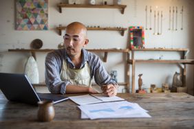 A small business owner sits at a table and looks at his laptop while working on his financial planning and bookkeeping.