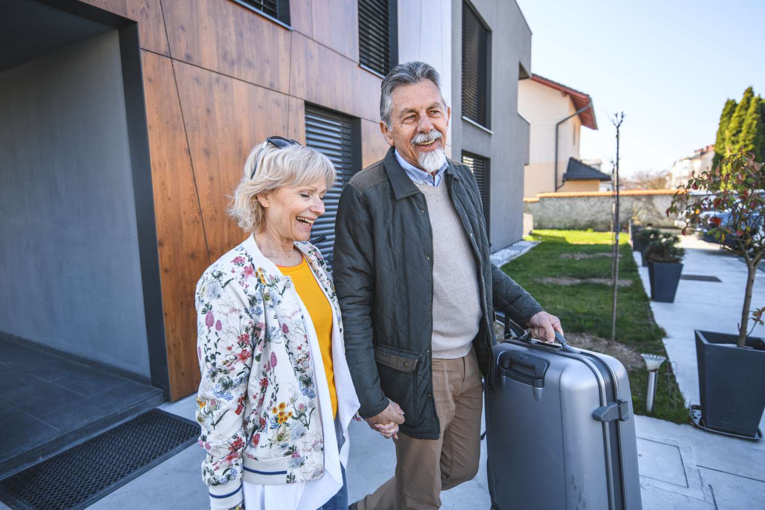 Senior couple holding hands and taking their luggage for a vacation, departing from their home.