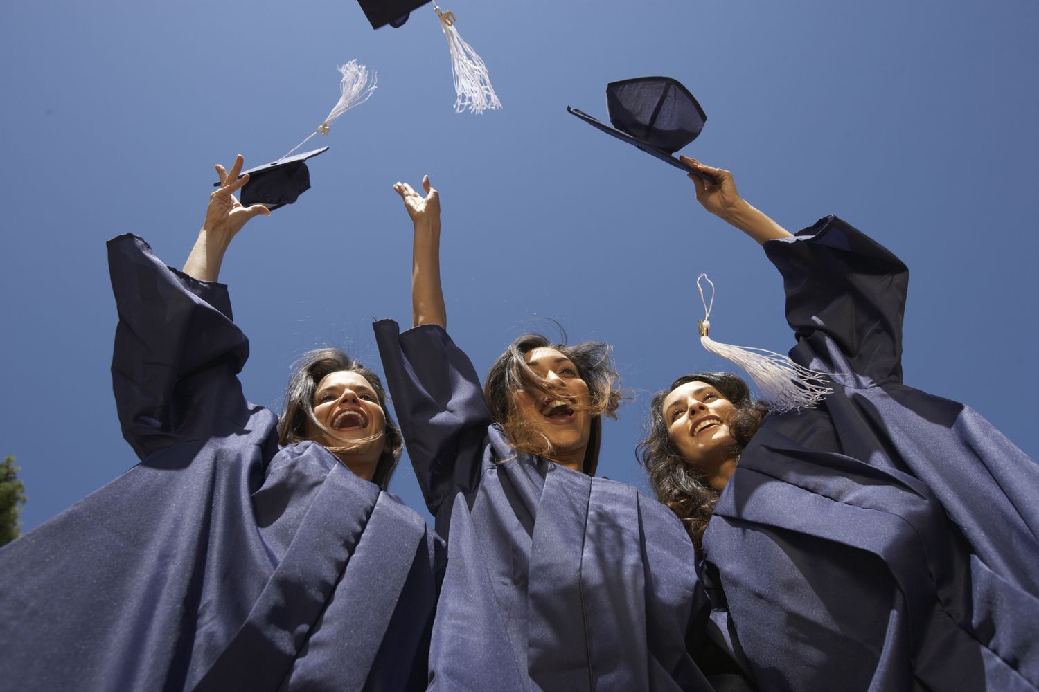 Three female graduate students throwing mortar boards, low angle view 