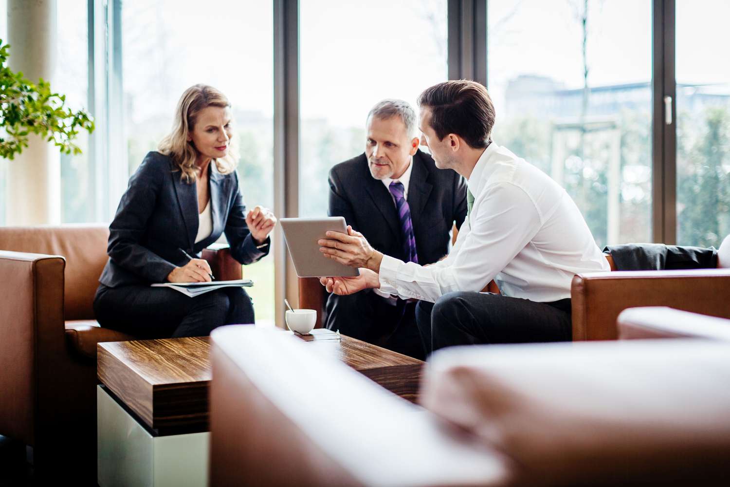 Three people meeting in an office, reviewing data on a digital tablet
