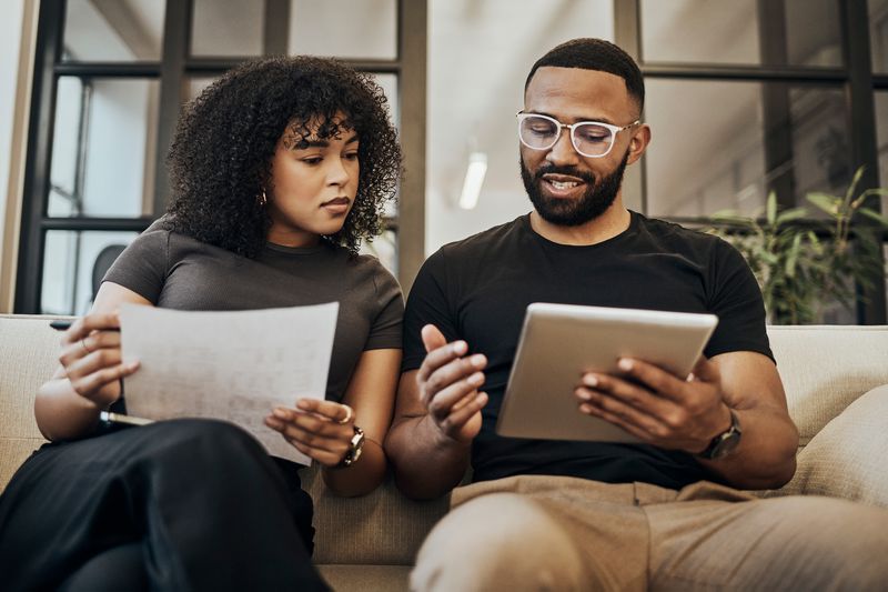 Young couple on a couch looking at a tablet and paperwork