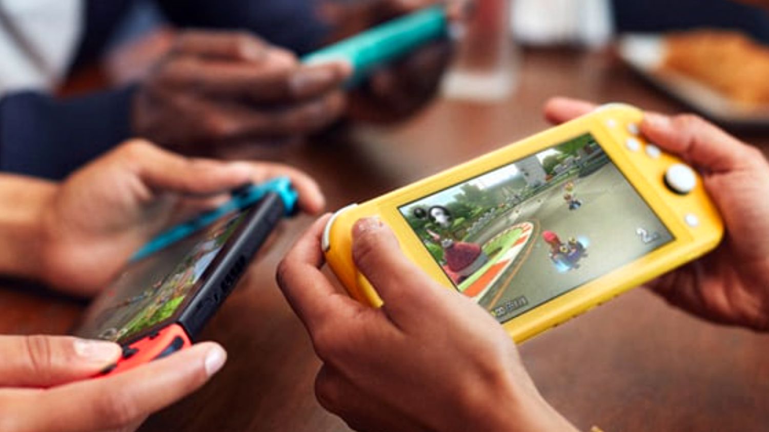 Three people playing Super Mario Kart 8 on a Nintendo Switch and two Nintendo Switch Lite consoles.