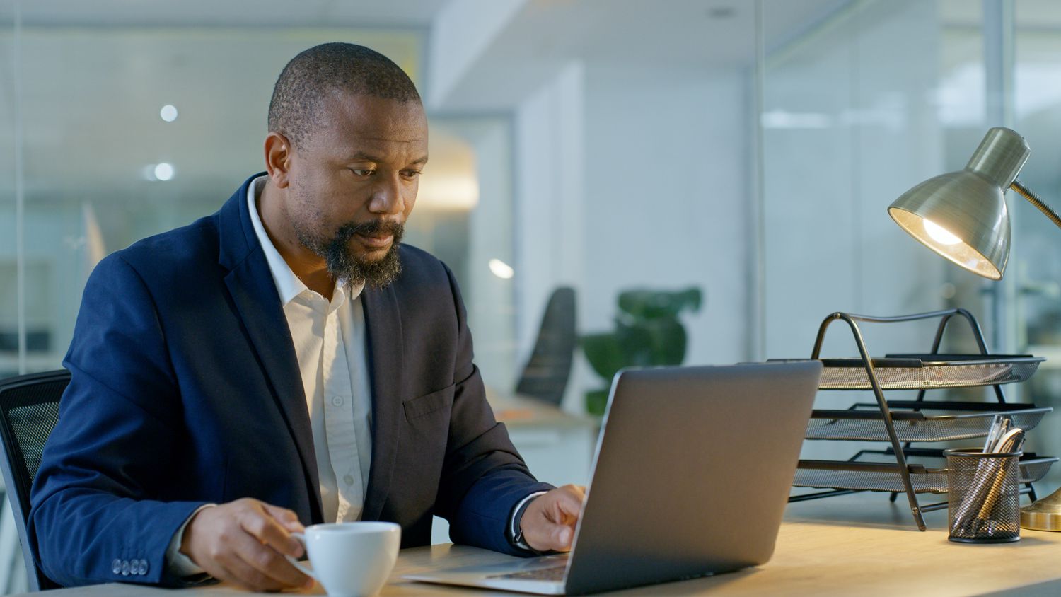 Man looking at his lap top while holding a tea cup