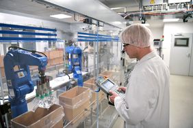 A conveyor belt and a worker operates a robot that transports insulin bags.