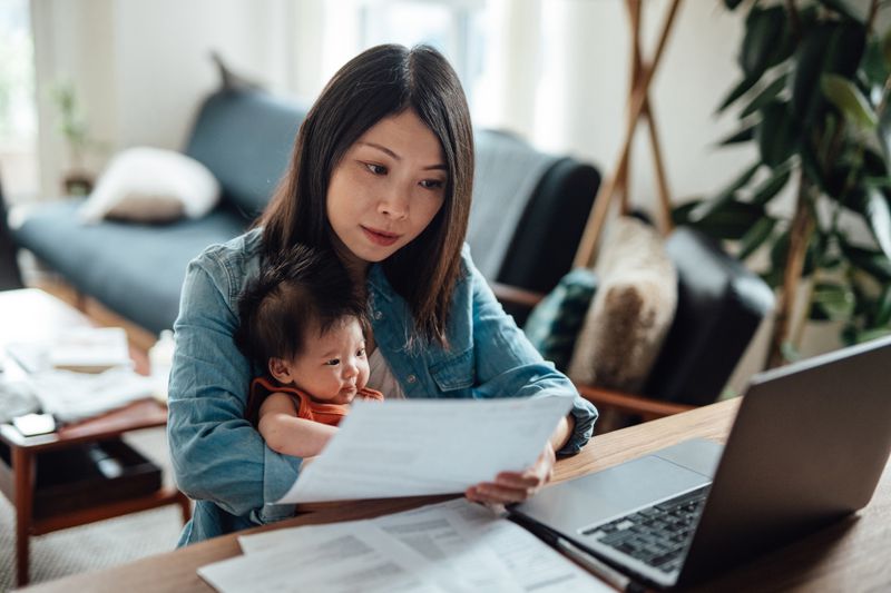 Asian women sitting down holding a baby girl in her arms while reviewing a paper in hand