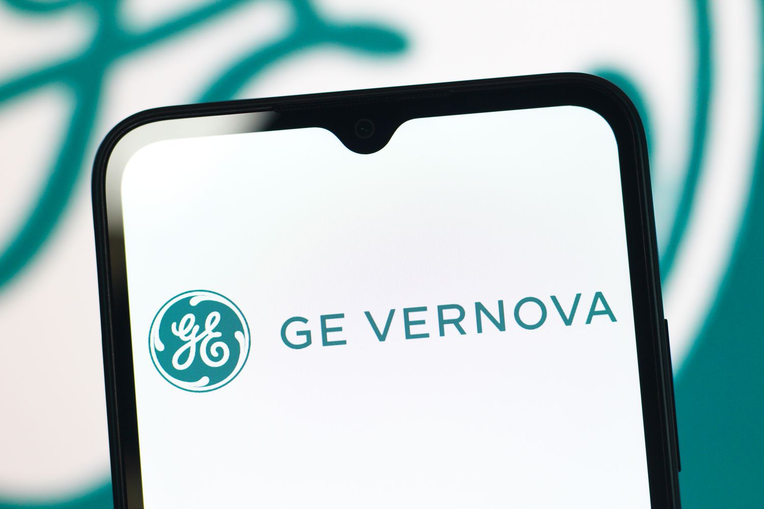 The green GE Vernova logo is seen on a phone screen, with a larger version in the background.