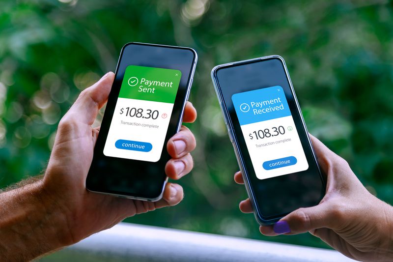 Two smartphones held by a woman and a man showing sending and receiving payments through a digital wallet application on a mobile phone. 
