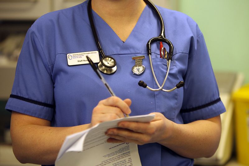 Nurse wearing blue scrubs takes notes. 