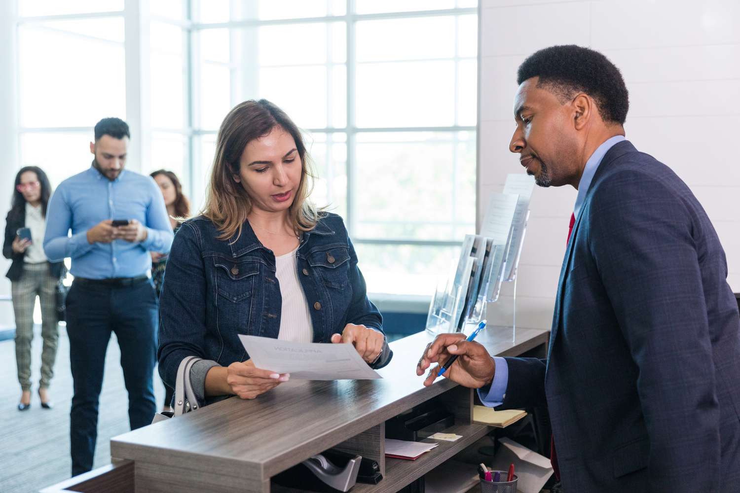 A male bank manager talks to a woman at the bank counter.