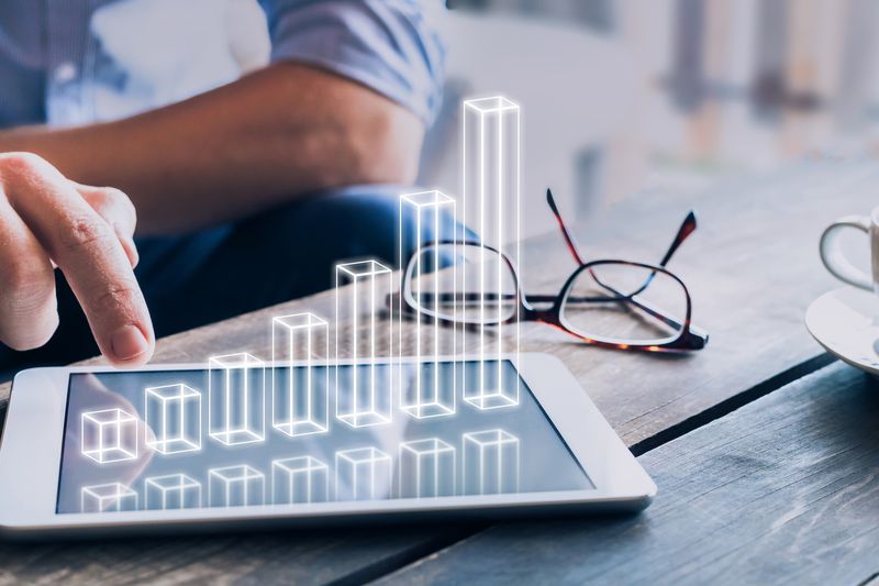 Businessman analyzing ascending 3D bar chart floating above digital tablet computer screen.