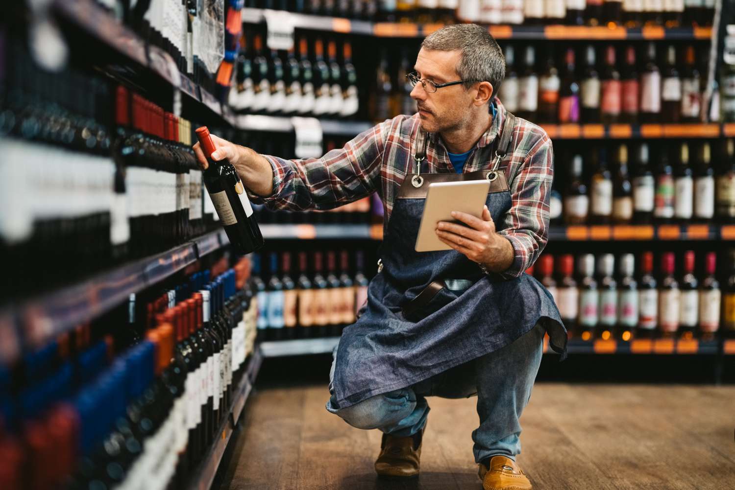A business owner checks the price of a bottle of wine on the shelf to ensure it is priced correctly.