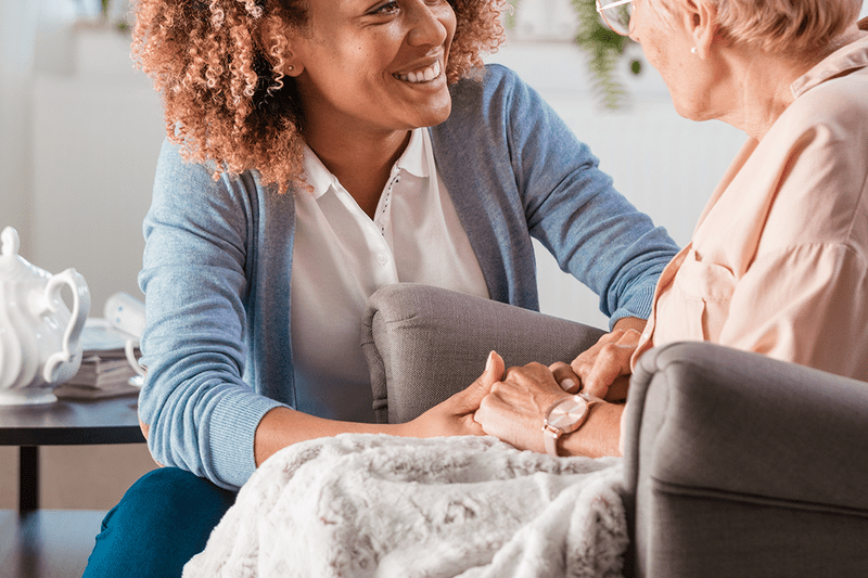 Young woman caring for older woman in armchair