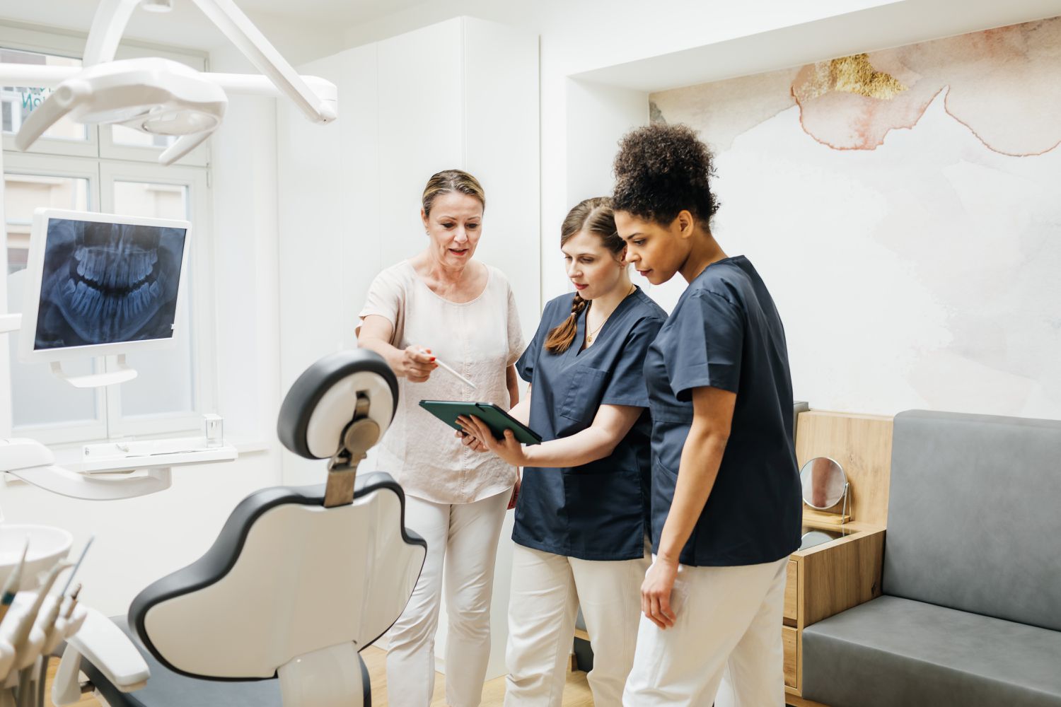 In a dental exam room, a woman reviews information on a tablet computer with a dentist and an assistant.