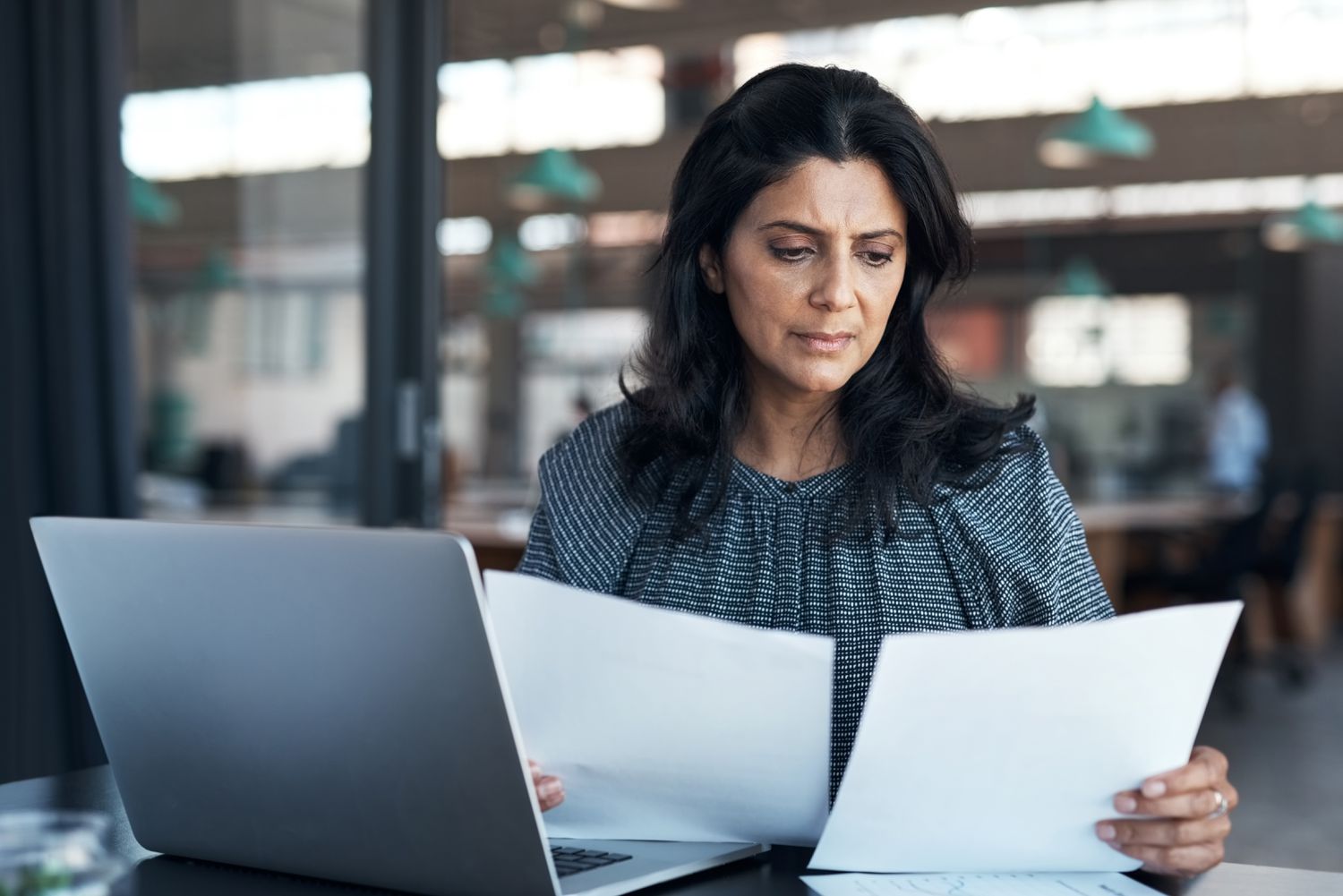 An investor sits at a desk with printed documents in their hands as they review the difference between investing in a Roth IRA account and a Traditional IRA account.
