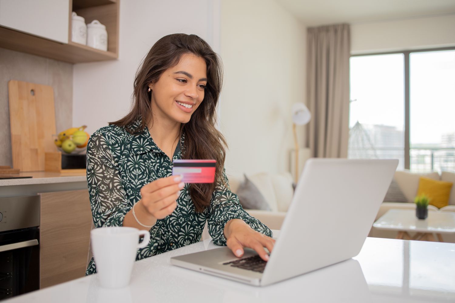 A woman opens a new bank account from her laptop while sitting at a table and holding up a debit card.