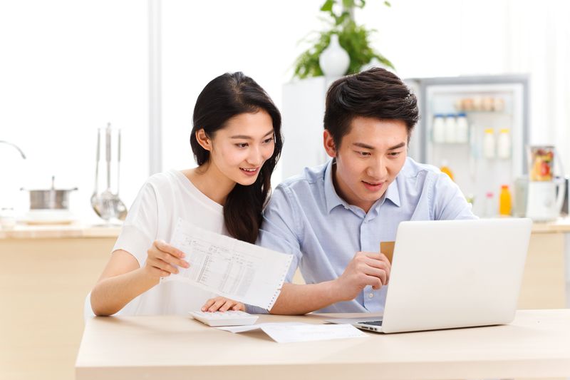 Young couple sitting in their kitchen and looking at financial documents a laptop