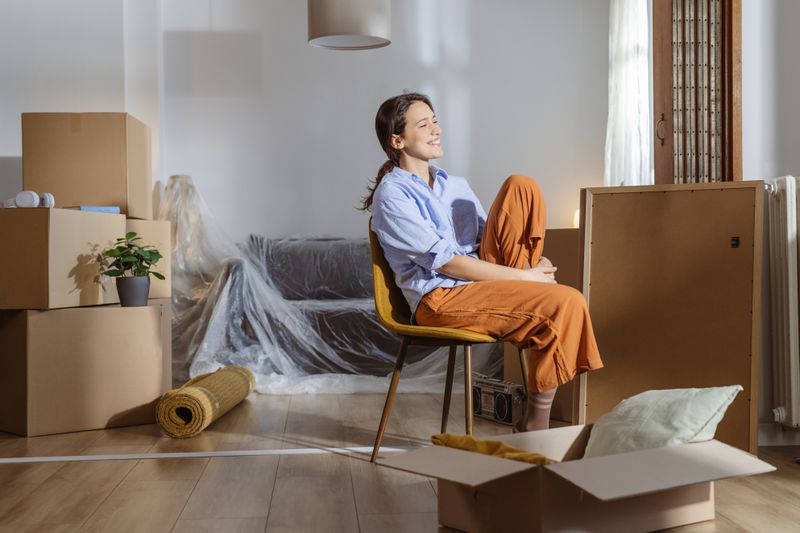 Cheerful happy young woman enjoying in her new apartment. She is surrounded by moving boxes and belongings