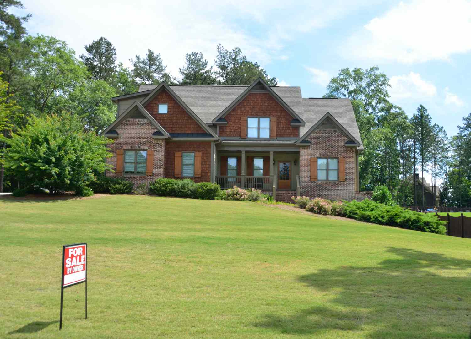 A brown house with a large yard and a for sale sign on the lawn