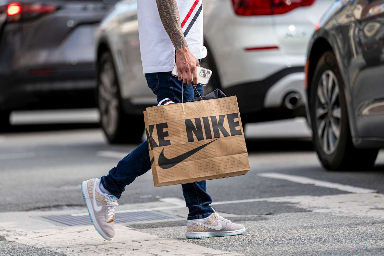 A person crosses the street wearing Nike shoes and carrying a Nike bag. 