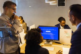 Office manager, technical specialist, and other coworkers discuss cybersecurity breech as a computer screen displays a system error message.