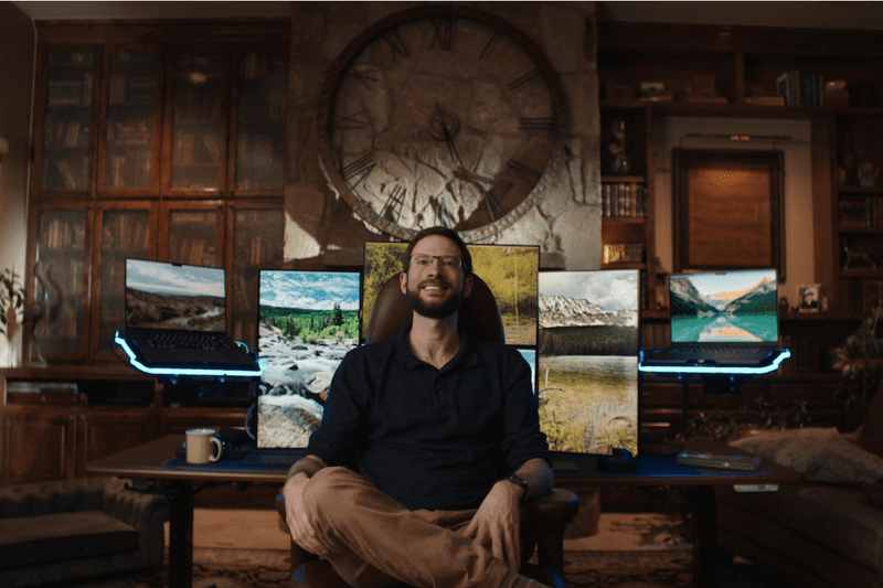 Person seated in front of a desk with multiple computer monitors in a room with a large wall clock