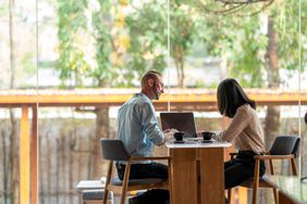 A financial advisor sits across the table from a client in a room with large windows. 