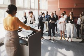 A marketing firm’s public relations person speaks from a podium to release positive company information to a select group of journalists. 
