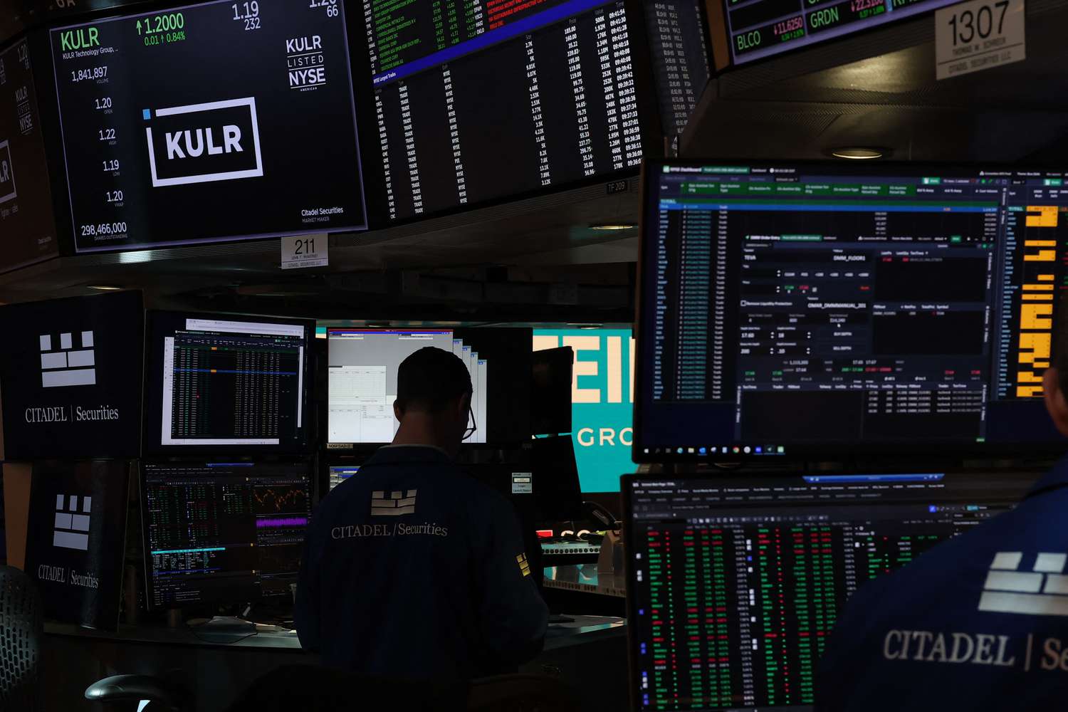 Traders working on a busy stock exchange floor surrounded by numerous monitors displaying financial data and stock information