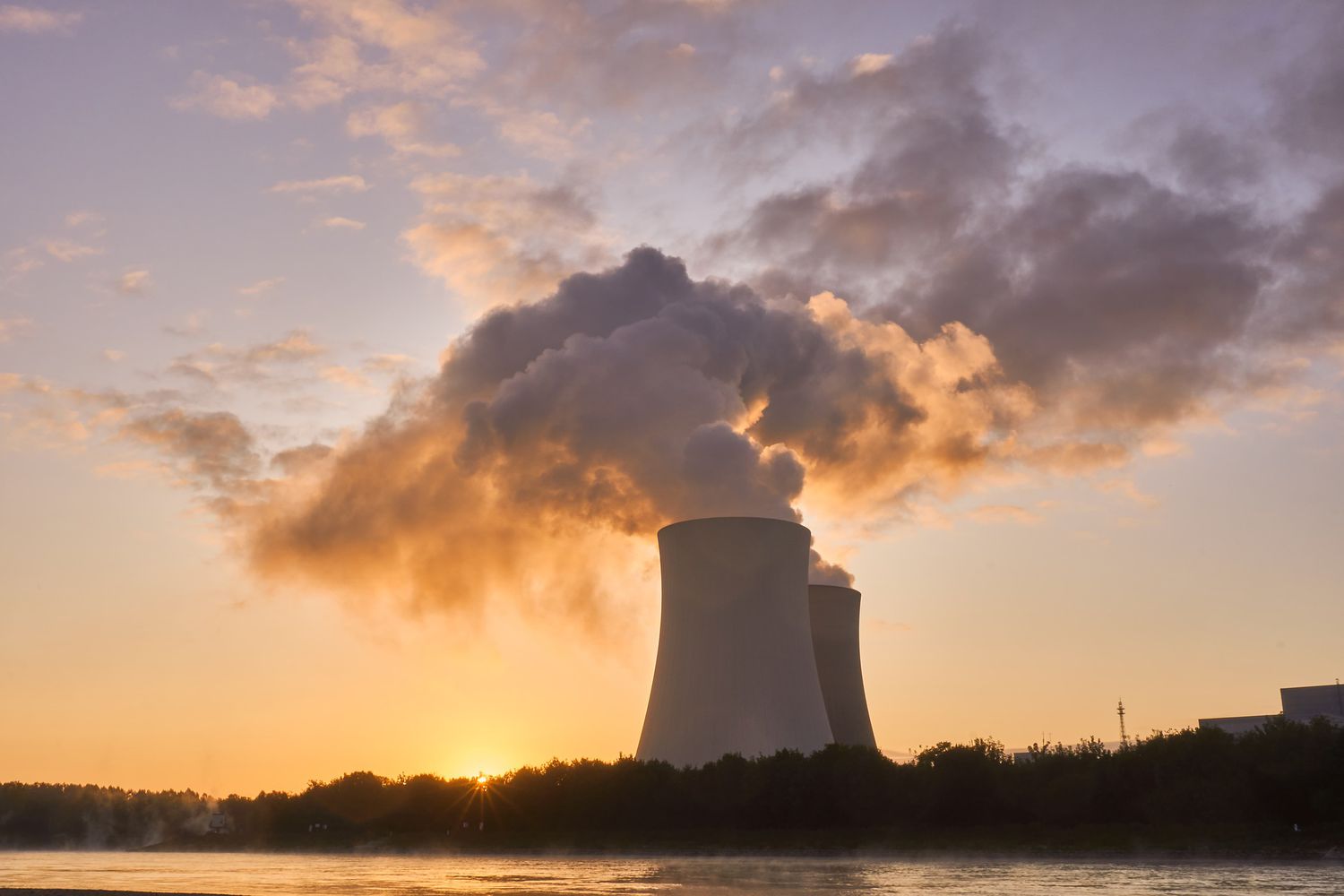 Steam clouds billowing into the sky coming from nuclear power plant at sunset