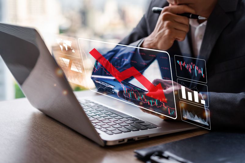 A person looks at stock documents with an arrow headed down.