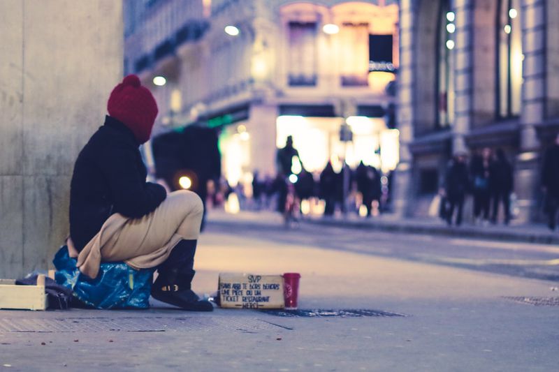 Homeless person sitting on city sidewalk, asking for money
