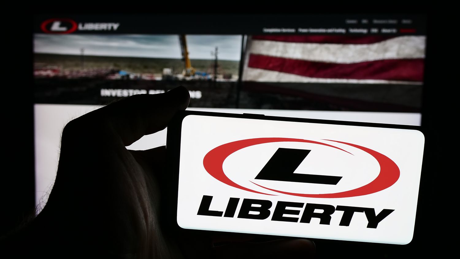 A person is holding a smartphone with the logo of US oilfield services company Liberty Energy Inc. in front of website