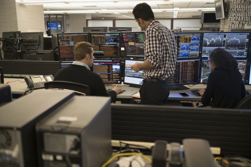 A team of three traders discuss strategies and trade execution in front of computer monitors displaying different information. 